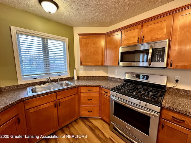 kitchen with appliances with stainless steel finishes, brown cabinetry, dark countertops, and a sink