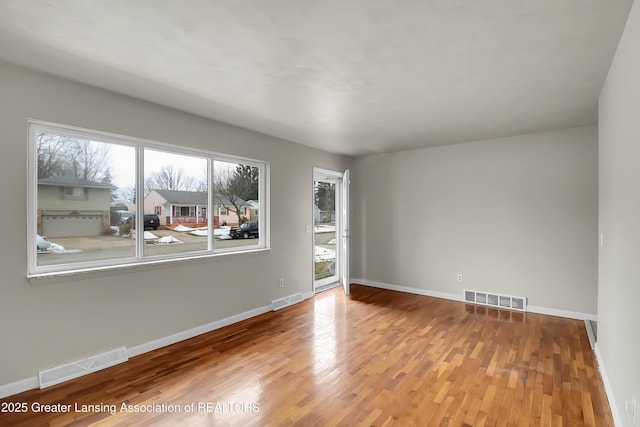 spare room with wood finished floors, visible vents, and baseboards