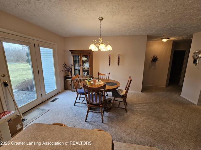 dining room with a chandelier, a textured ceiling, carpet flooring, visible vents, and baseboards