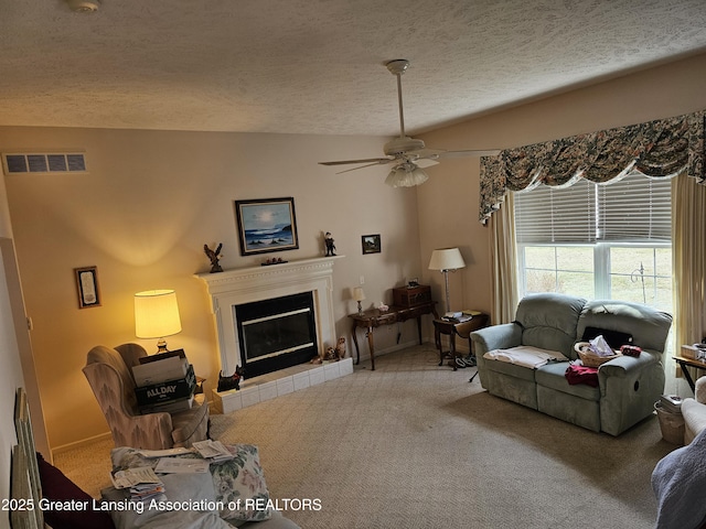 carpeted living room featuring a textured ceiling, ceiling fan, visible vents, baseboards, and a tiled fireplace