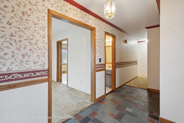 corridor with dark colored carpet, stone finish floor, crown molding, and wallpapered walls