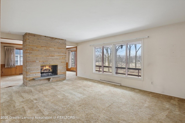 unfurnished living room with carpet, a baseboard radiator, a wealth of natural light, and a stone fireplace