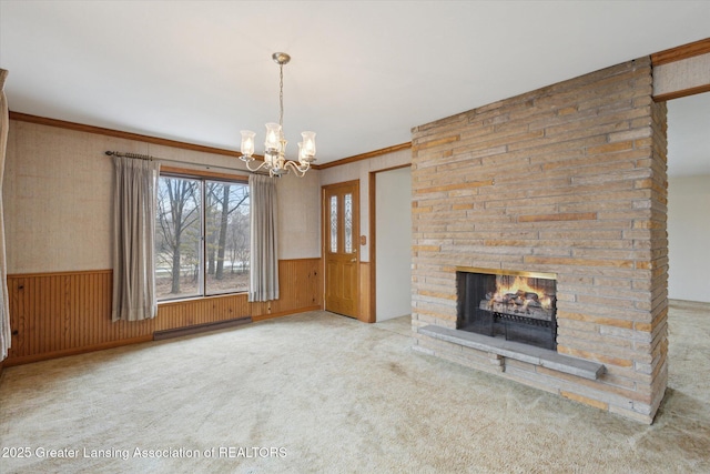 unfurnished living room featuring carpet, a fireplace, crown molding, wainscoting, and a chandelier