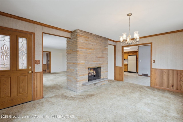 unfurnished living room featuring carpet floors, a wainscoted wall, a fireplace, ornamental molding, and a chandelier