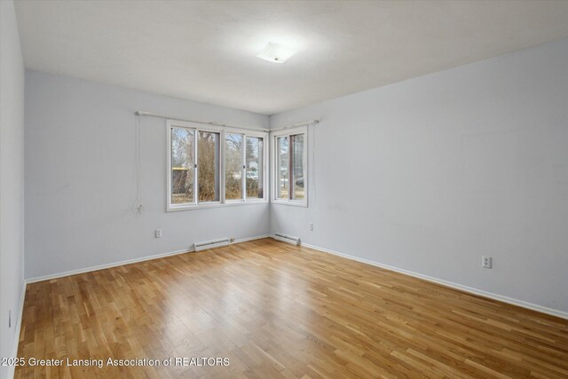 empty room featuring baseboards, a baseboard radiator, and light wood-style floors