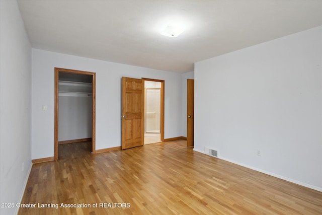 unfurnished bedroom with visible vents, baseboards, a walk in closet, light wood-type flooring, and a closet