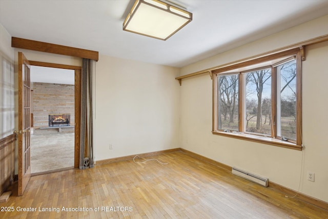 unfurnished room with light wood-style floors, baseboards, baseboard heating, and a stone fireplace