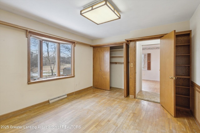 unfurnished bedroom with baseboard heating, a closet, and light wood-style flooring