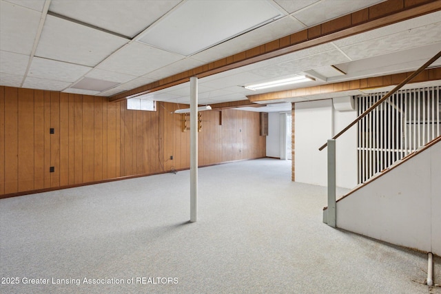 basement featuring wood walls, stairway, and a drop ceiling