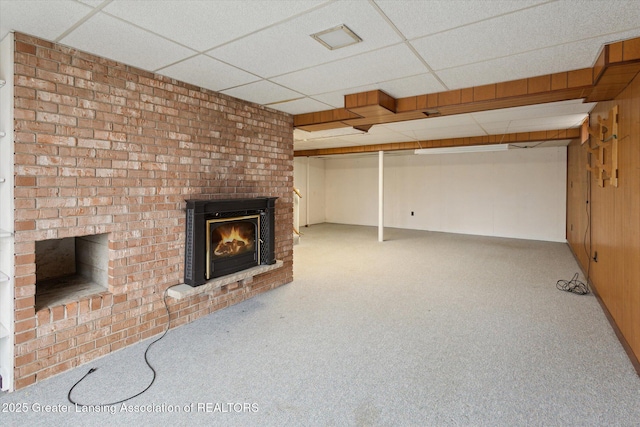 unfurnished living room featuring carpet, a drop ceiling, and a brick fireplace