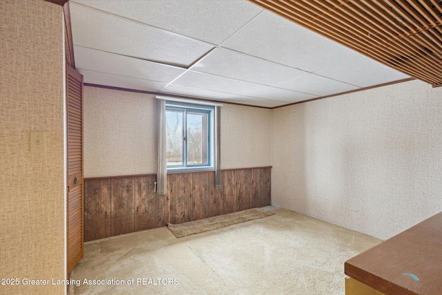 carpeted spare room with a wainscoted wall, a paneled ceiling, and wooden walls