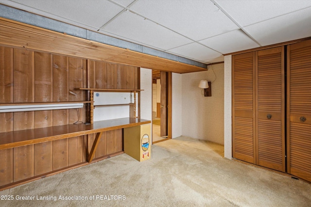 interior space featuring built in desk, a drop ceiling, and carpet flooring