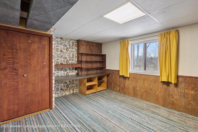 interior space with a paneled ceiling, wood walls, carpet, and wainscoting