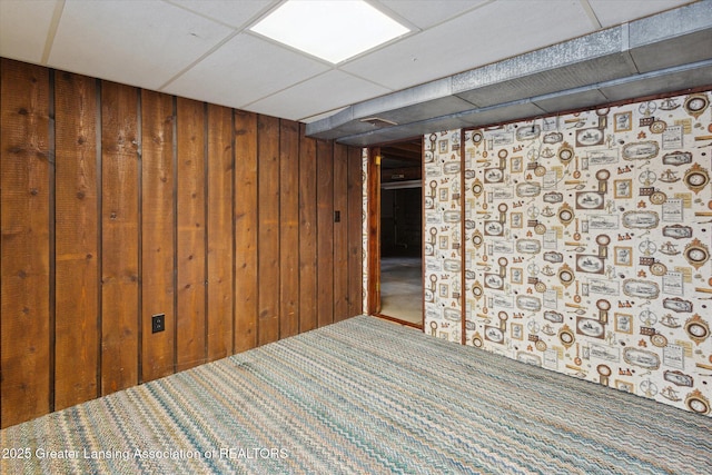 finished below grade area featuring wood walls, carpet, and a paneled ceiling