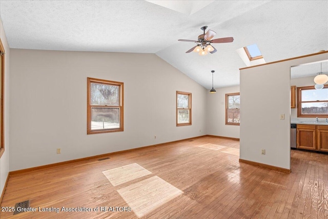 unfurnished living room with light wood-style flooring, lofted ceiling with skylight, a sink, a textured ceiling, and ceiling fan