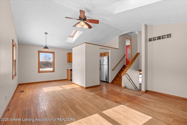 unfurnished living room with light wood-style floors, visible vents, stairway, and lofted ceiling with skylight