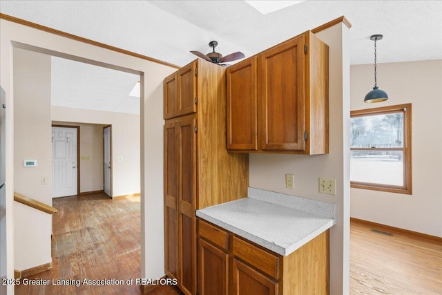 kitchen featuring light countertops, light wood-type flooring, decorative light fixtures, and brown cabinets