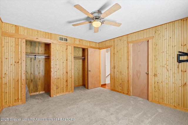 unfurnished bedroom featuring visible vents, a textured ceiling, carpet floors, wood walls, and two closets