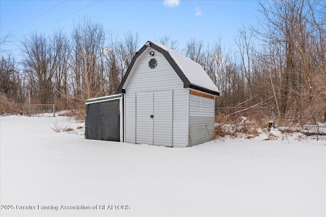 snow covered structure with an outdoor structure, a barn, and fence