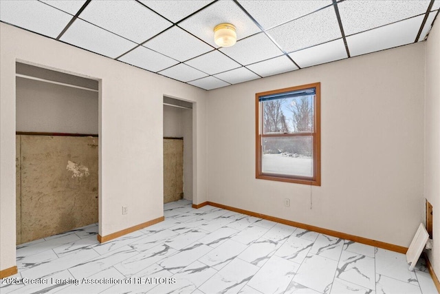 unfurnished bedroom with multiple closets, marble finish floor, and a drop ceiling