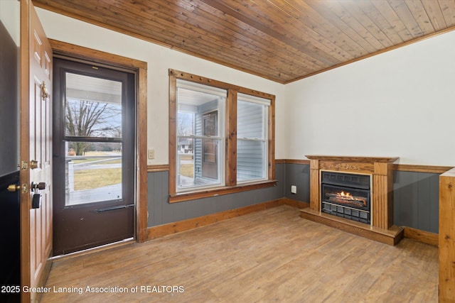 unfurnished living room featuring wooden ceiling, a lit fireplace, wood finished floors, and wainscoting