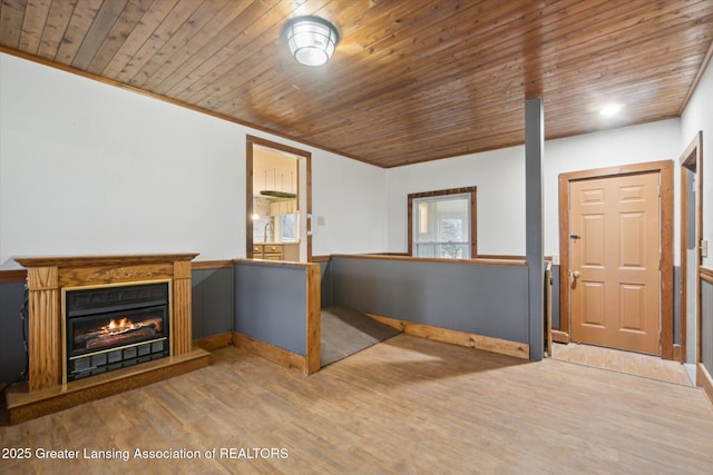 unfurnished living room featuring a warm lit fireplace, baseboards, wooden ceiling, wood finished floors, and crown molding