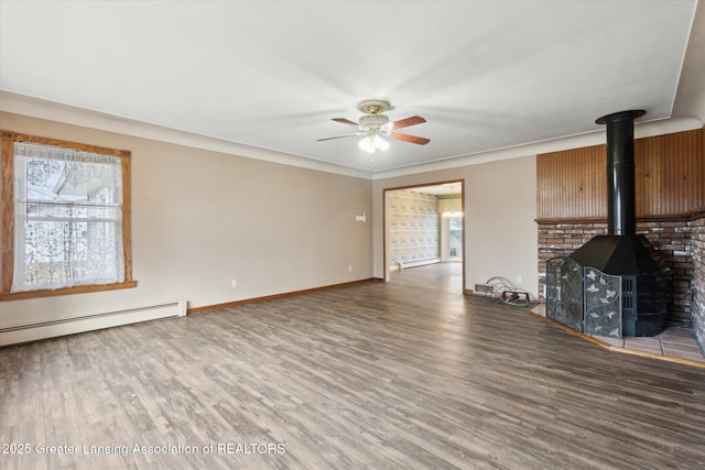 unfurnished living room featuring baseboard heating, a ceiling fan, a wood stove, wood finished floors, and baseboards