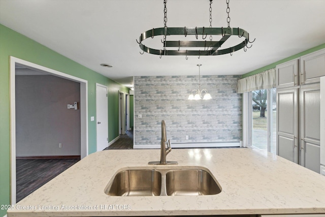 kitchen featuring baseboards, light stone counters, dark wood-style flooring, decorative light fixtures, and a sink