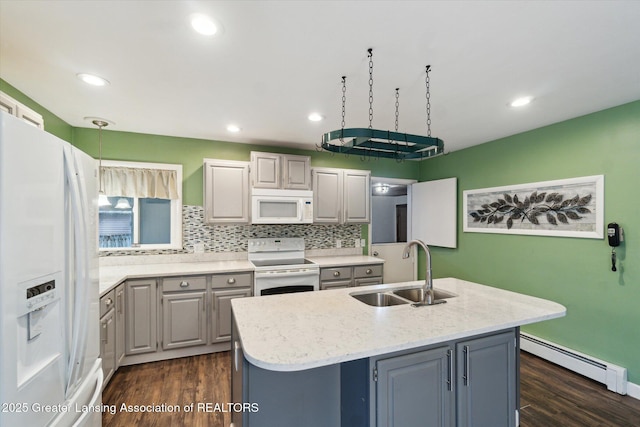 kitchen featuring white appliances, a sink, baseboard heating, gray cabinets, and a center island with sink