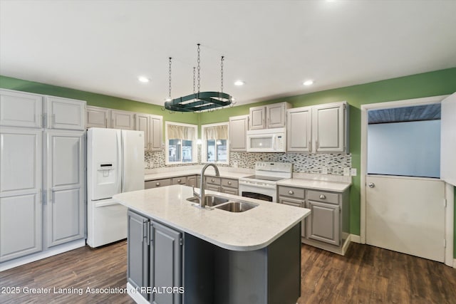 kitchen featuring white appliances, a center island with sink, dark wood-type flooring, gray cabinetry, and a sink