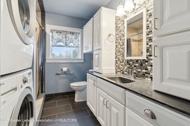 bathroom featuring tasteful backsplash, stacked washer and clothes dryer, toilet, a shower with curtain, and vanity