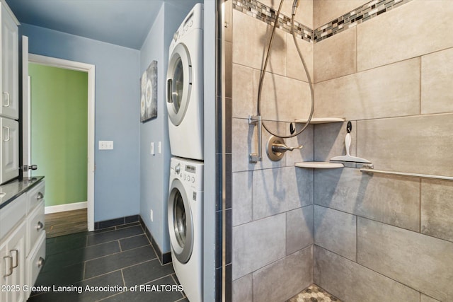 washroom with stacked washer / drying machine, laundry area, dark tile patterned floors, and baseboards