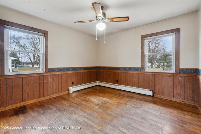 spare room with a ceiling fan, wainscoting, wood walls, and wood finished floors