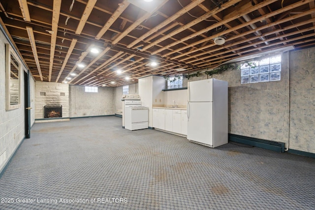 basement with a baseboard radiator, freestanding refrigerator, carpet floors, a fireplace, and a sink