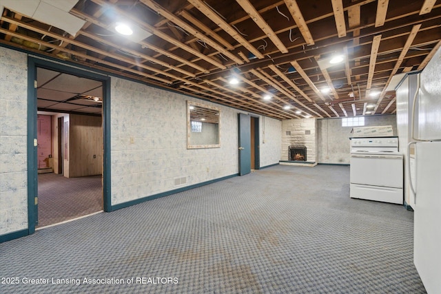 below grade area featuring carpet floors, a fireplace, visible vents, and freestanding refrigerator