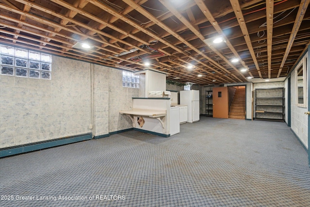 basement featuring a baseboard heating unit, a wealth of natural light, stairs, and freestanding refrigerator