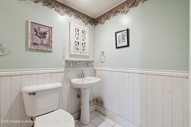 bathroom with tile patterned flooring, wainscoting, a sink, and toilet