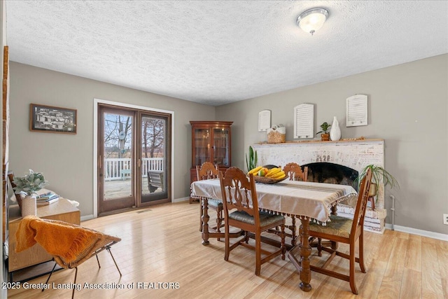 dining space with a textured ceiling, a fireplace, light wood-style flooring, and baseboards