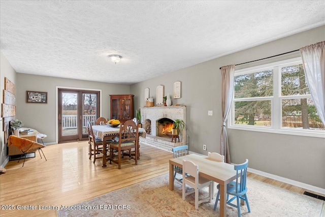 dining room featuring a brick fireplace, visible vents, light wood-style flooring, and a healthy amount of sunlight