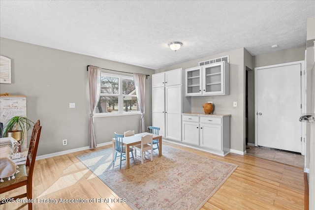 dining area featuring a textured ceiling, light wood-type flooring, and baseboards