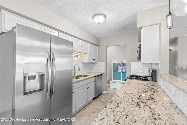 kitchen with decorative backsplash, light stone counters, stainless steel appliances, a textured ceiling, and a sink