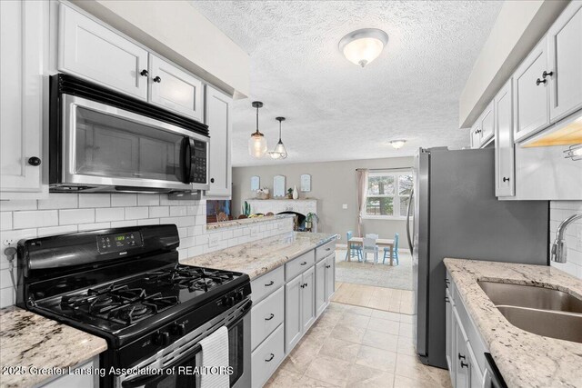 kitchen with a sink, decorative backsplash, gas range, stainless steel microwave, and decorative light fixtures