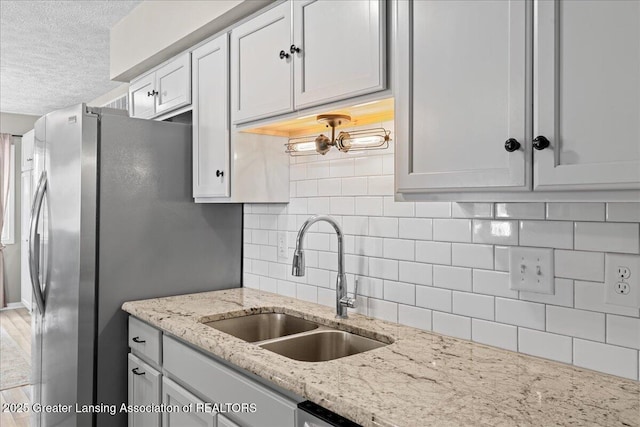 kitchen with a textured ceiling, light stone counters, a sink, white cabinets, and tasteful backsplash