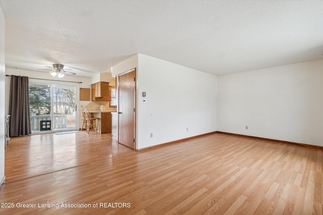 unfurnished living room with light wood-type flooring, ceiling fan, baseboards, and a textured ceiling