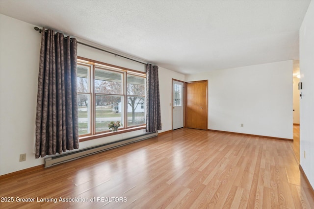 empty room with a baseboard heating unit, light wood-type flooring, a textured ceiling, and baseboards