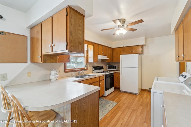 kitchen with washer and clothes dryer, light countertops, a sink, white appliances, and a peninsula