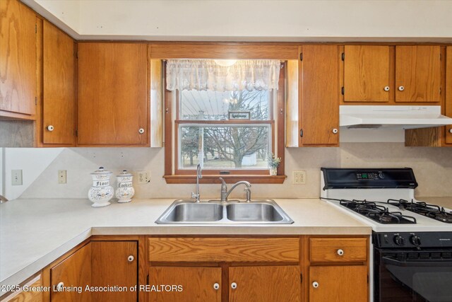 kitchen featuring light countertops, brown cabinetry, a sink, gas range, and under cabinet range hood