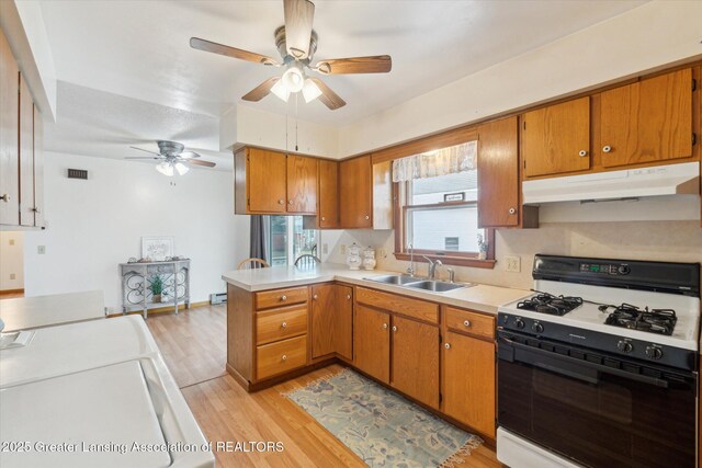 kitchen with range with gas stovetop, light countertops, brown cabinetry, a sink, and under cabinet range hood