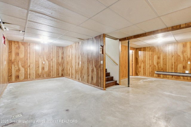 finished basement featuring a paneled ceiling, wood walls, and stairway