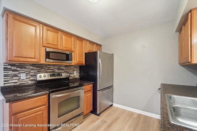 kitchen featuring light wood finished floors, tasteful backsplash, stainless steel appliances, and a sink